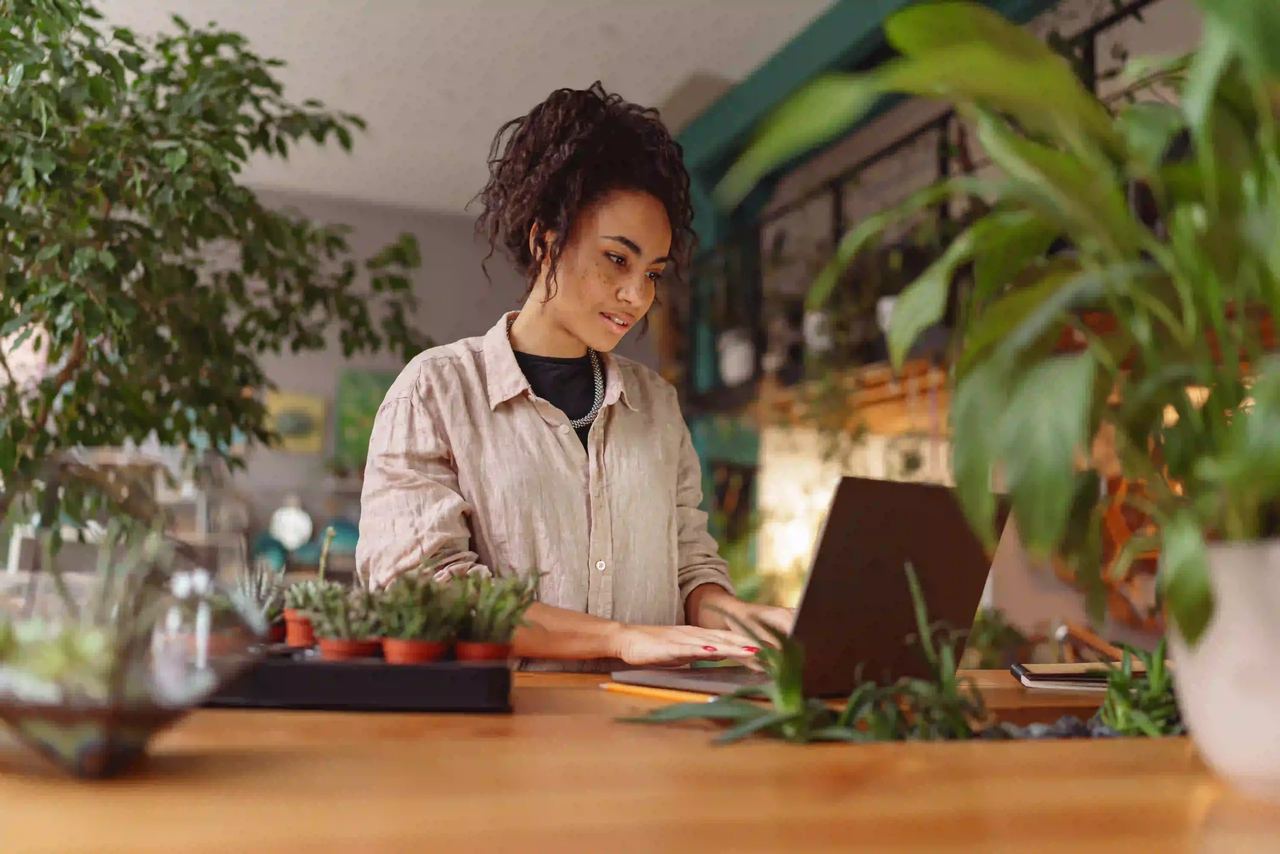 Inhaberin eines Geschäfts arbeitet zwischen Pflanzen am Laptop